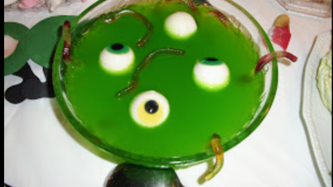 Eine grüne Halloween-Bowle mit Augen und Gummiwürmern zieht die Aufmerksamkeit auf sich, perfekt für eine festliche Stimmung.
