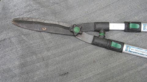 Eine Heckenschere liegt auf einer grauen Unterlage, bereit zur Reparatur, um den Hebelarm wieder funktionsfähig zu machen.