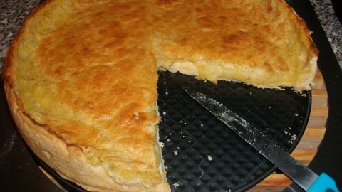 Ein goldbrauner Schwäbischer Kartoffelkuchen steht auf einem Tisch, während ein Stück mit einem Messer herausgeschnitten wird.