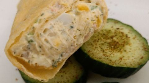 Ein knuspriger Wrap mit cremiger Füllung liegt neben gewürzten Gurkenscheiben als erfrischende Beilage.