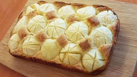 Ein saftiger Apfelkuchen mit schön geschnittenen Äpfeln und knusprigem Rand liegt auf einem Holzteller.
