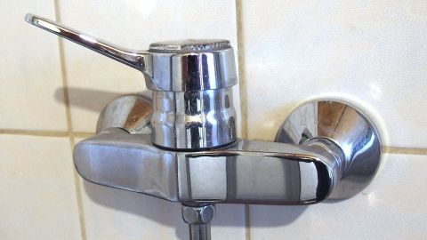 Ein glänzender Wasserhahn glänzt in einer gefliesten Dusche und zeigt mögliche Kalkflecken, die mit Stahlwolle entfernt werden können.