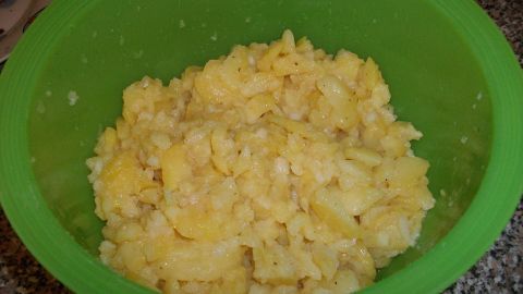 Ein grüner Schüssel mit schwäbischem Kartoffelsalat, der cremig wirkt, steht auf einer Arbeitsplatte in der Küche.