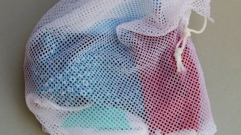 Masken aus Baumwollstoff mit Nasenbügel schonend waschen, mithilfe eines Wäschenetzes. Ein Netzsack enthält farbige Stoffmasken, die vorsichtig in der Waschmaschine gereinigt werden sollen.