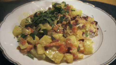 Ein appetitlicher Karotten-Kohlrabi-Kartoffel-Auflauf wird auf einem weißen Teller serviert, garniert mit frischen Kräutern.