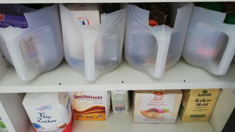 Vorratsbehälter aus Kanistern stehen ordentlich in einem Regal und enthalten verschiedene Lebensmittel in durchsichtigen Behältern.