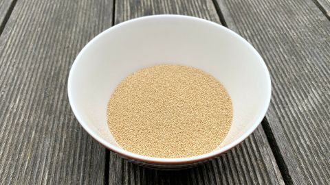 Ein Schüsselchen mit gepufftem Amaranth steht auf einer Holzoberfläche, die grob strukturiert ist und natürlich aussieht.