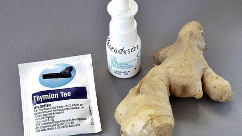 Ein Nasenspray und ein Stück frischer Ingwer liegen neben einem Beutel Thymian-Tee auf grauem Untergrund.