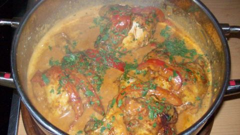 Geröstetes Paprika-Hähnchen wird in einem Topf mit einer cremigen Sauce gar gekocht, umgeben von frischem Gemüse und Kräutern.