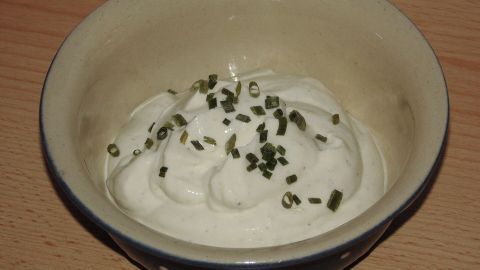Ein Dip aus Joghurt und Kräutern wird in einer Schale serviert, umgeben von einer holzartigen Tischoberfläche.
