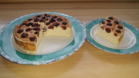 Ein Quark-Kirsch-Kuchen auf einem großen Teller, ein Stück fehlt, daneben ein kleinerer Teller mit dem Stück.