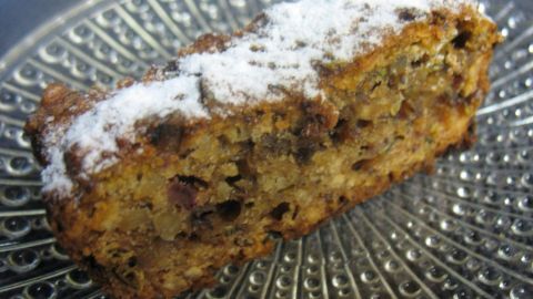 Ein veganer Zucchini-Nuss-Kuchen, auf einem silbernen Teller präsentiert, ist mit Puderzucker bestäubt.