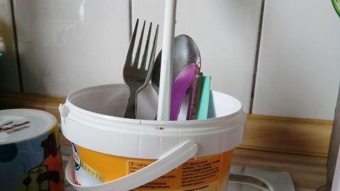 Ein großer Joghurt-Behälter steht in einer Küche und enthält Besteck wie Löffel und Gabel, die ordentlich sortiert sind.