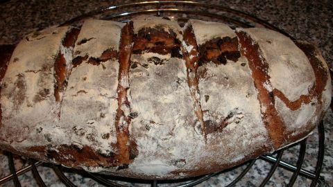Ein frisch gebackenes Zwiebel-Bauernbrot ruht auf einem Gitter, während der feine Mehlsack die Kruste bedeckt.