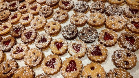 Leckere Linzer Augen liegen auf einem Tisch, einige mit Puderzucker bestreut, während sie zum Verzehr bereit sind.