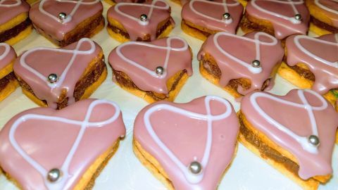 Herzförmige Punsch-Herzen liegen in einer Reihe, überzogen mit rosa Zuckerguss und verziert mit silbernen Kügelchen.