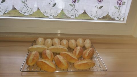 Weizen-Baguettebrötchen liegen frisch auf einem Gitter, während Tageslicht durch ein Fenster strömt.