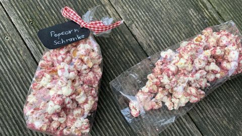 Two Tüten mit Red Velvet Cake Popcorn stehen auf einer Holzoberfläche, dekoriert mit einem karierten Band und beschriftet.