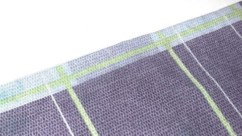 Mit einem Trick sieht die nicht ganz knitterfreie Tischdecke auf dem Tisch aus wie frisch gebügelt. Eine sauber liegende Tischdecke zeigt eine glatte Oberfläche mit lila und grünen Streifen auf einem hellen Tisch.