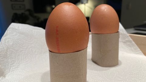 Zwei Eier stehen auf Eierbechern aus Papierrollen, auf Küchenpapier, in einer gemütlichen Umgebung mit sanfter Beleuchtung.