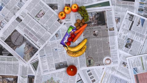 Auf einem Haufen Zeitungen liegen frische Lebensmittel, während sie eine Frage zu Ernährung symbolisieren.