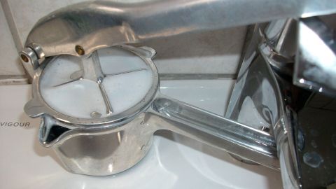 Ein silberner Entsafter steht auf einer weißen Arbeitsfläche und wird benutzt, um frischen Saft zu pressen.
