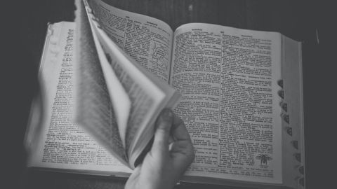 Ein aufgeschlagenes Wörterbuch mit einer Hand, die durch die Seiten blättert, um alte deutsche Wörter zu entdecken.