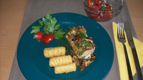 Gefülltes Schweinerückensteak liegt auf einem blauen Teller, umgeben von Pommes und frischem Salat in einer Schüssel.