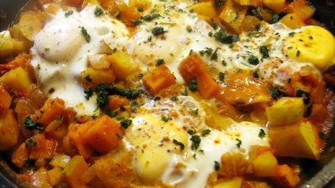 Eine bunte Schmorpfanne mit Kürbis und Kartoffeln, garniert mit Eiern und Kräutern, frisch auf dem Herd zubereitet.