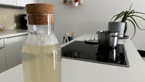 Eine nach hinten geneigte Glasflasche mit corkdeckel zeigt frischen, hellen Apfel-Birnen-Saft in einer modernen Küche.