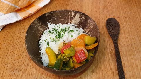Ein tiefes Schälchen mit duftendem, buntem Gemüse-Curry und fluffigem Reis, auf einem Holztisch angerichtet.