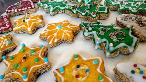 Bunte, weiche Lebkuchen in Form von Sternen und Weihnachtsbäumen liegen auf einem hellen Tisch und sind kunstvoll verziert.