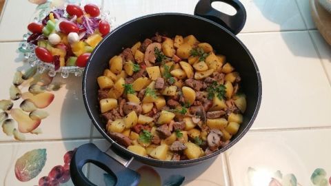 Eine schmackhafte marokkanische Lammpfanne mit Kartoffeln und Fleischstücken wird in einer Pfanne zubereitet, umgeben von frischem Salat.