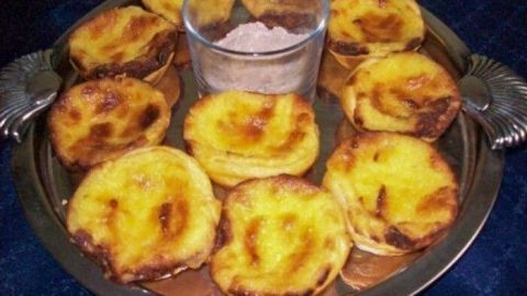 Zarte Pasteis de Belem sind auf einem silbernen Tablett angerichtet, umgeben von einer Schüssel mit Zucker.