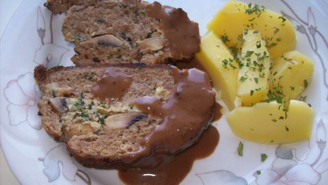 Ein gefüllter Hase aus Hackfleisch, mit Kräutern und Champignons, liegt auf einem Teller neben Kartoffeln.