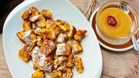 Kaiserschmarrn liegt auf einem weißen Teller, umgeben von Apfelmus, das mit einem Klecks Fruchtmark garniert ist.