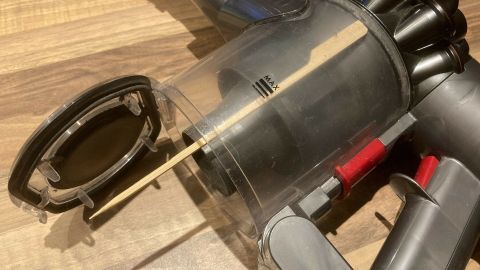 Der Akku-Handstaubsauger mit geöffnetem Behälter zeigt, wie man ihn entleert, auf einem Holzfußboden.
