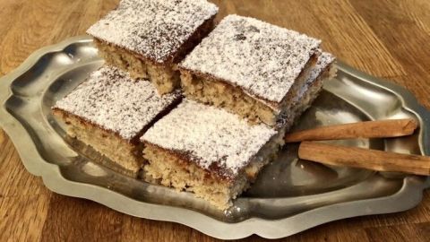 Ein platter Lebkuchen-Kuchen ist auf einem Silbertablett angeordnet, bestäubt mit Puderzucker und umgeben von Zimtstangen.