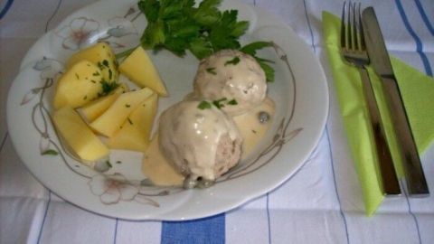 Auf einem Teller liegen saftige Kalbfleisch-Klöße in cremiger Sauce, begleitet von Kartoffelstücken und frischer Petersilie.