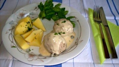 Auf einem Teller liegen saftige Kalbfleisch-Klöße in cremiger Sauce, begleitet von Kartoffelstücken und frischer Petersilie.