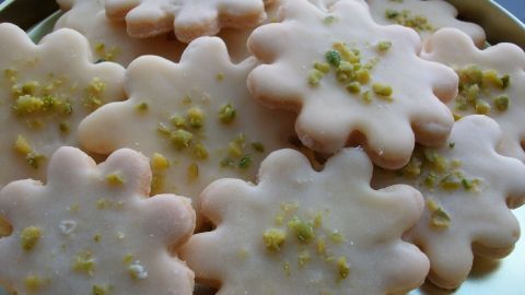 Die plätzchenförmigen Eierlikör-Plätzchen liegen auf einem goldenen Teller, glasiert mit Zuckerguss und mit Pistazienstückchen verziert.