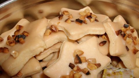 Sternförmige Rum-Sterne-Plätzchen liegen in einer Metallbox und sind mit gehackten Nüssen dekoriert.