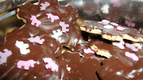 Süße Plätzchen mit Schokoguss liegen in einer Schüssel, dekoriert mit bunten Einhornstreuseln in Form von kleinen Einhörnern.
