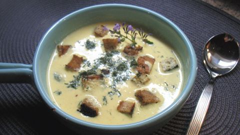 Eine Schüssel mit cremiger Senfsuppe, garniert mit Kräutern und Brotwürfeln, steht auf einem eleganten Untersetzer.