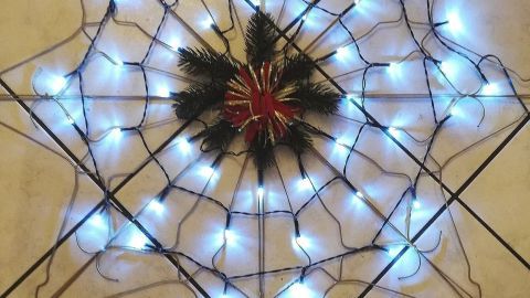 Ein Stern aus Kleiderbügeln leuchtet mit blauen Lichtern und ist mit einem festlichen Schmuckmittel in der Mitte dekoriert.
