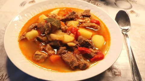 Ein gefüllter Teller Kesselgulasch mit zartem Fleisch, Kartoffeln und Paprika in einer würzigen Brühe auf einem Tisch.
