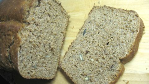 Ein frisch geschnittenes rustikales Roggen-Weizen-Vollkornbrot liegt auf einem Holzbrett und zeigt eine dichte, körnige Textur.