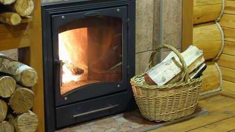 Ein Kamin mit flammendem Feuer steht im Raum, daneben ein Korb mit Holz, um die Wärme zu genießen.