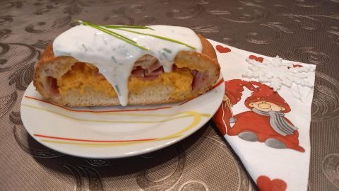 Ein Handbrot liegt auf einem Teller, gefüllt mit Eiern und Schinken, mit Sauce und Schnittlauch dekoriert, neben einer Serviette.