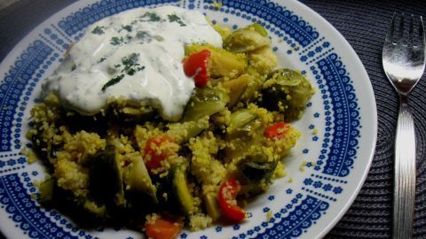Ein bunter Teller mit Couscous, Rosenkohl und Gemüse wird von einer Joghurtsoße begleitet, auf einem blauen Muster.